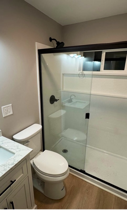 Bathroom with a sliding glass shower door, white surround, toilet and white vanity