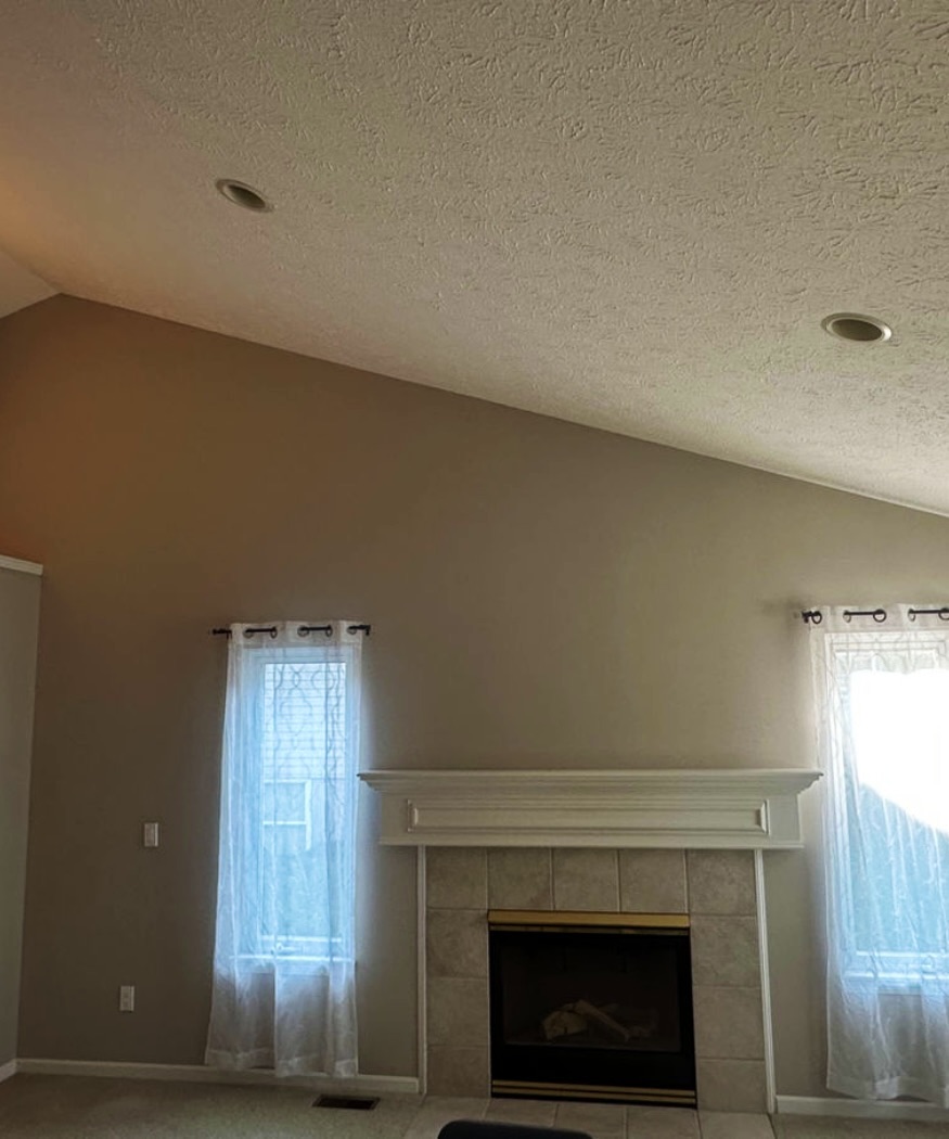 Living room with a white fireplace mantel, tall window and freshly painted walls